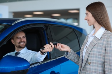 Photo of Saleswoman giving key to client inside new car in salon, selective focus