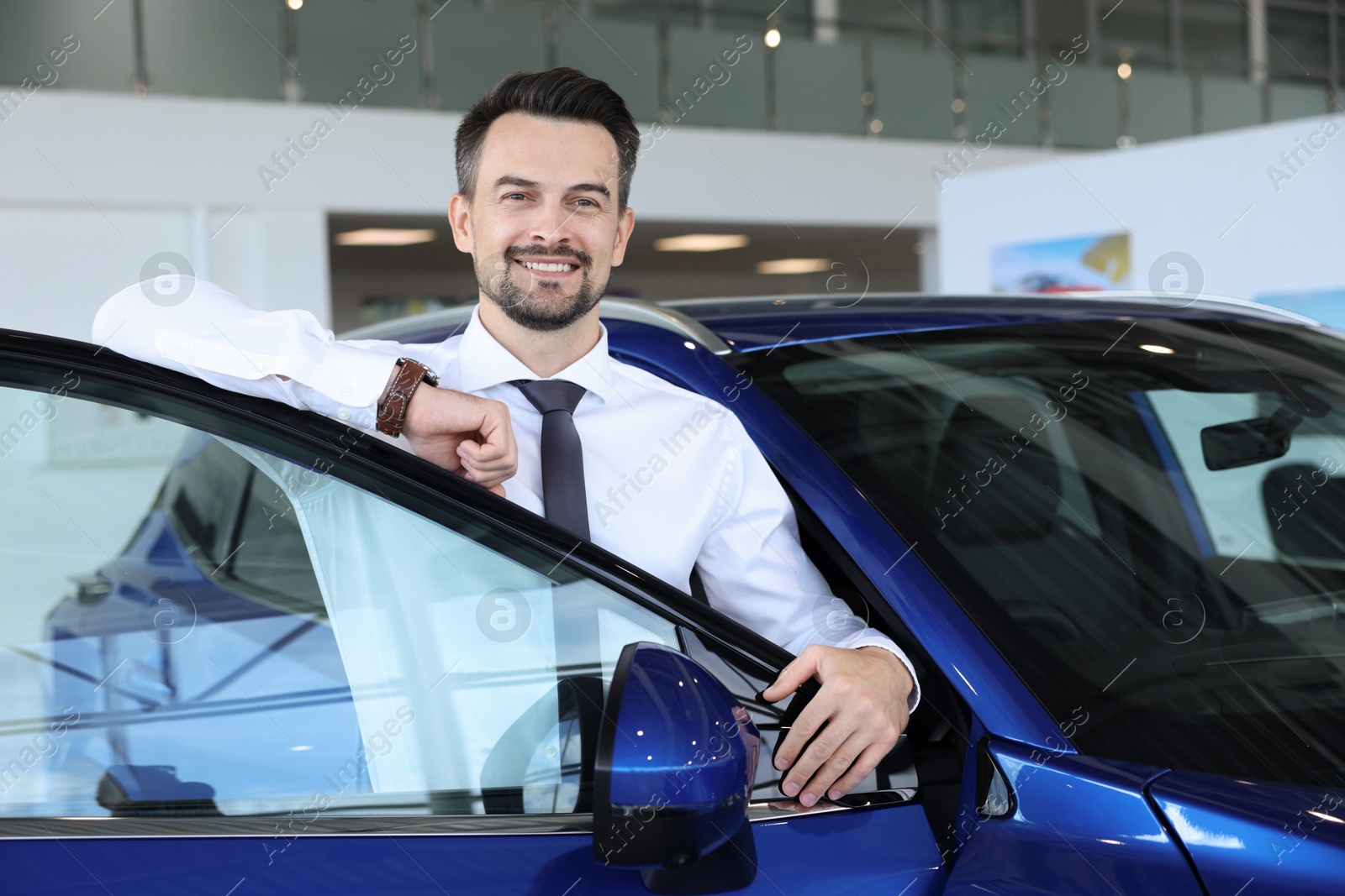 Photo of Happy man near new blue car in salon