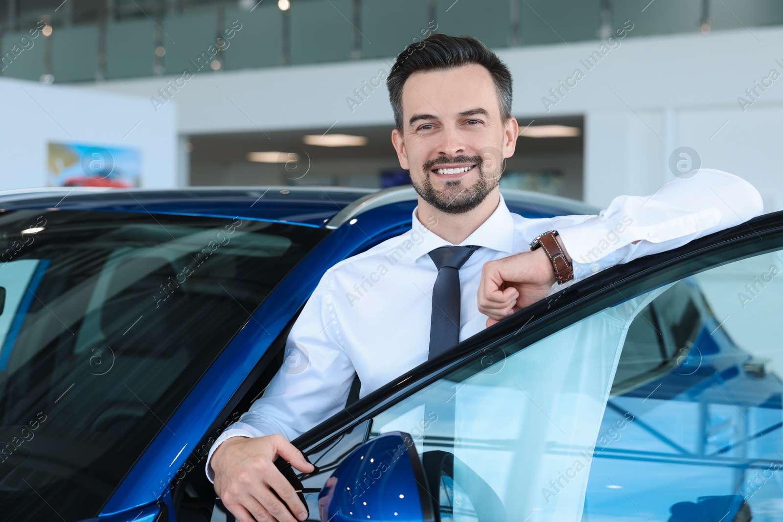 Photo of Happy man near new blue car in salon