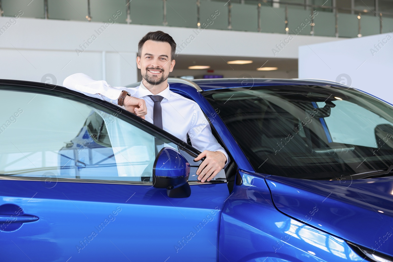 Photo of Happy man near new blue car in salon