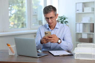 Photo of Middle aged man with smartphone at table in office