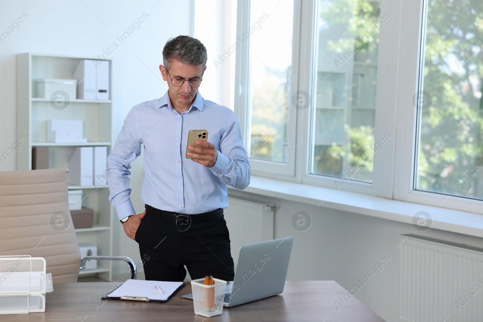 Photo of Middle aged man using smartphone in office. Space for text