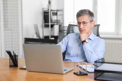 Photo of Middle aged man working with laptop at table in office