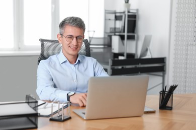 Photo of Smiling middle aged man working with laptop at table in office