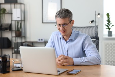 Photo of Middle aged man working with laptop at table in office