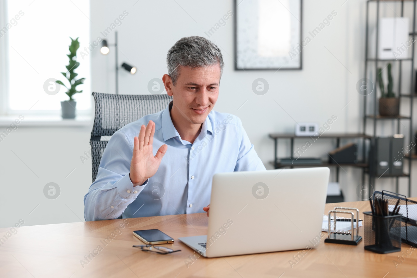 Photo of Smiling middle aged man having videochat via laptop at table in office