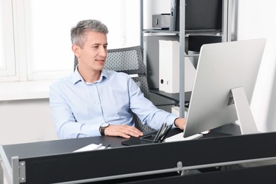 Photo of Middle aged man working with computer at table in office