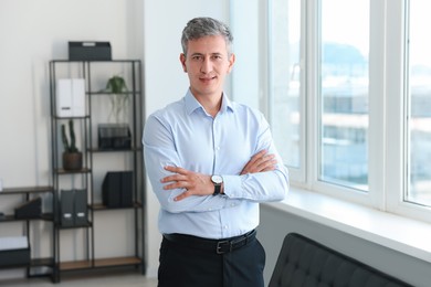 Photo of Portrait of smiling middle aged man with crossed arms in office