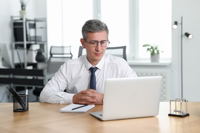 Photo of Middle aged man working with laptop at table in office