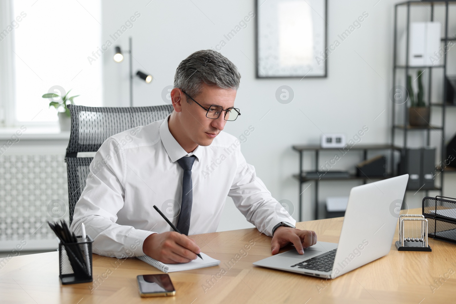 Photo of Middle aged man working with laptop at table in office