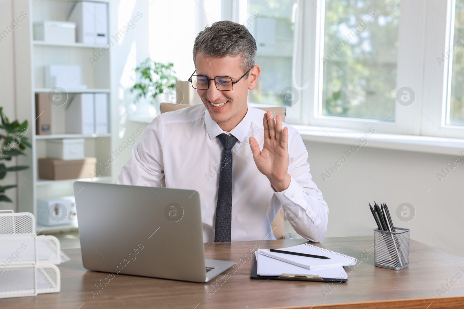 Photo of Smiling middle aged man having videochat via laptop at table in office