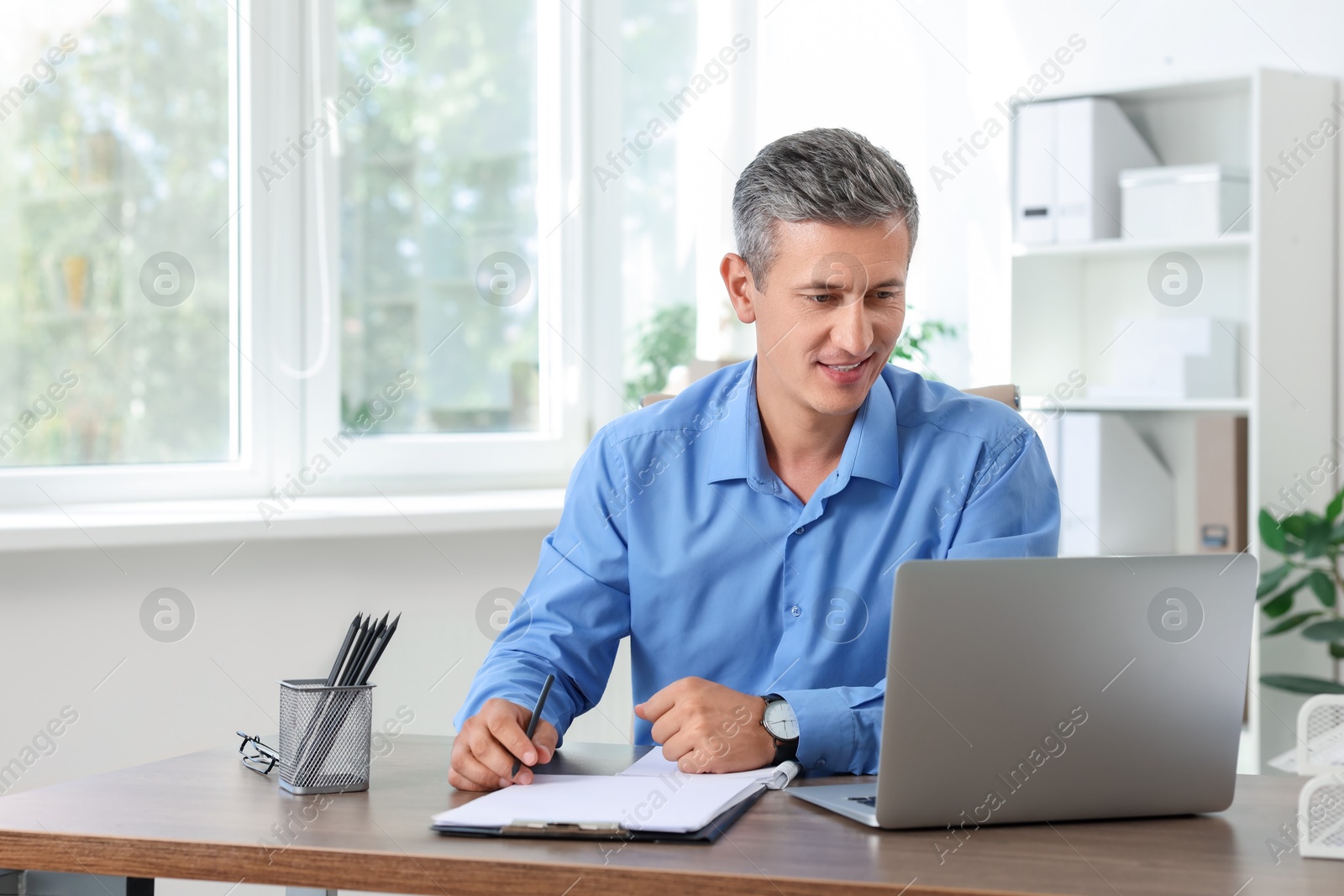 Photo of Smiling middle aged man working with laptop at table in office