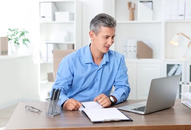 Photo of Middle aged man working with laptop at table in office