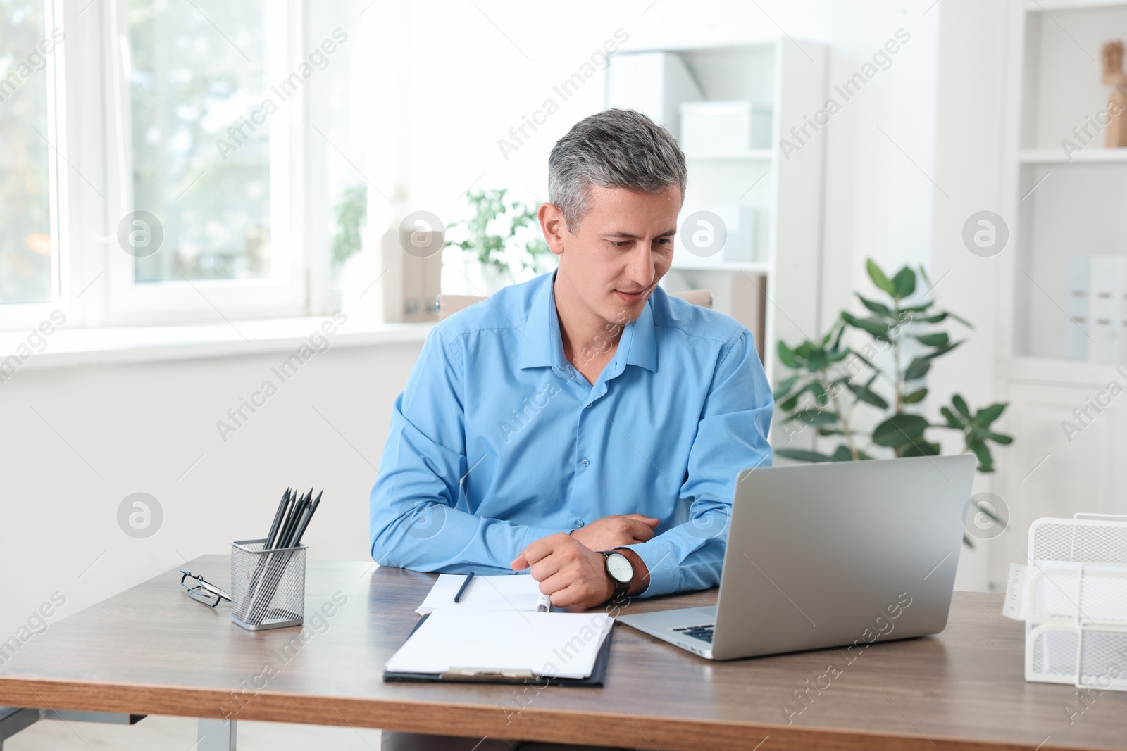 Photo of Middle aged man working with laptop at table in office