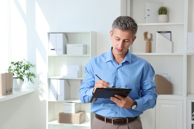 Photo of Middle aged man writing on clipboard in office. Space for text