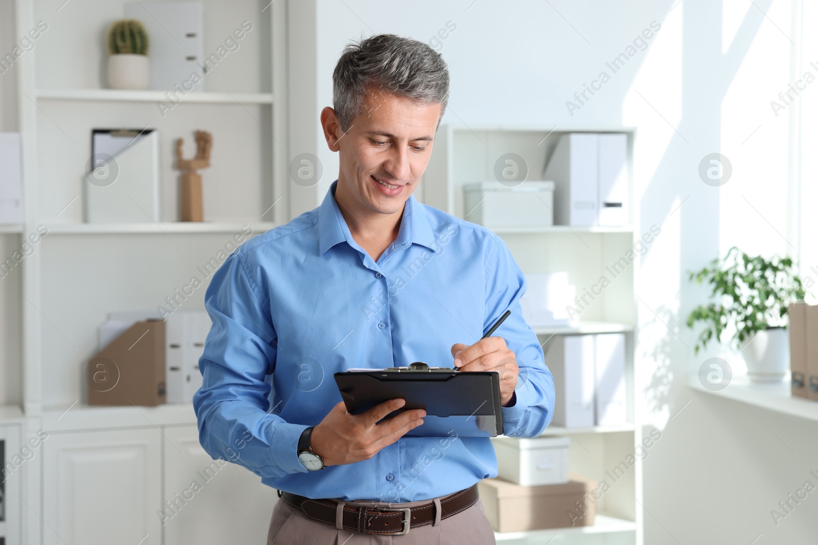 Photo of Smiling middle aged man writing on clipboard in office