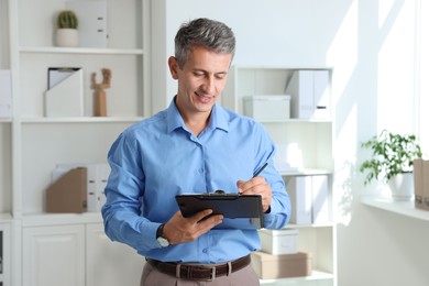 Photo of Smiling middle aged man writing on clipboard in office