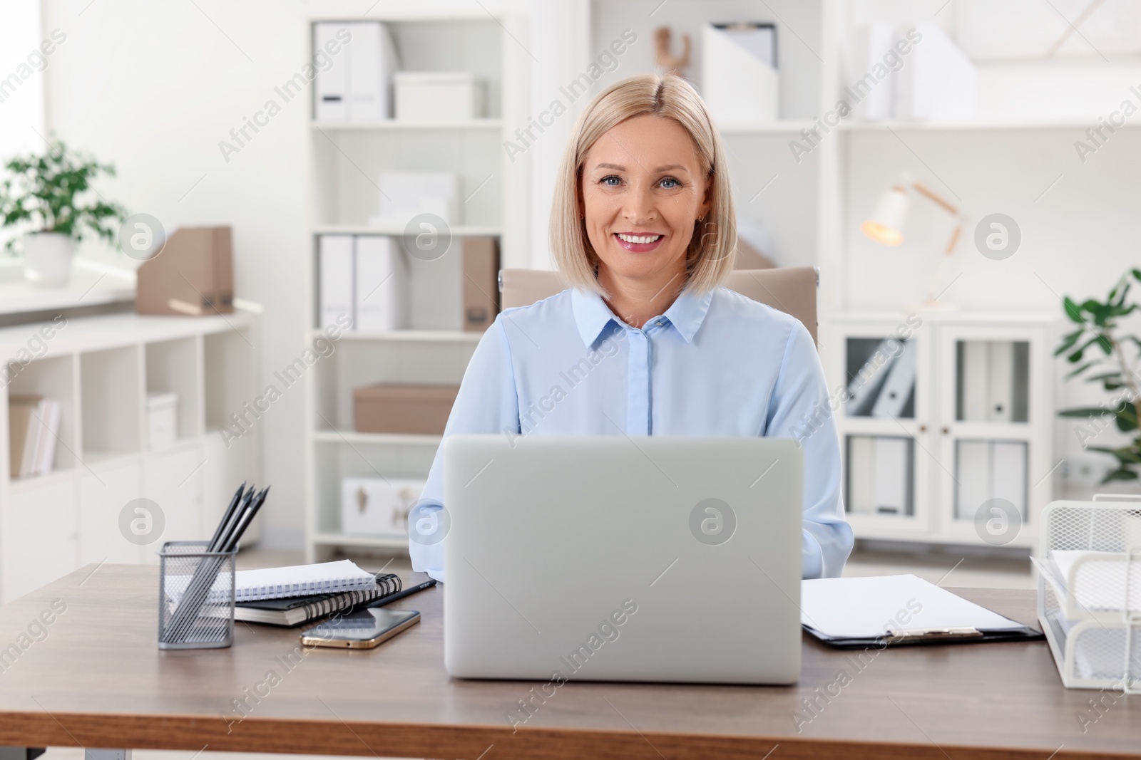 Photo of Smiling middle aged woman at table with laptop in office