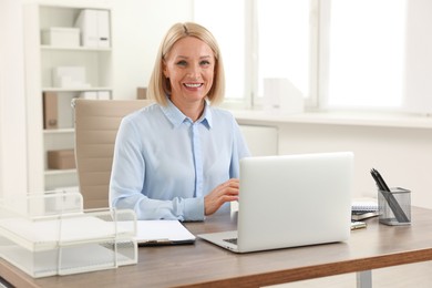 Photo of Smiling middle aged woman at table with laptop in office