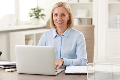 Photo of Smiling middle aged woman working with laptop at table in office