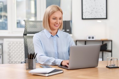 Photo of Smiling middle aged woman working with laptop at table in office