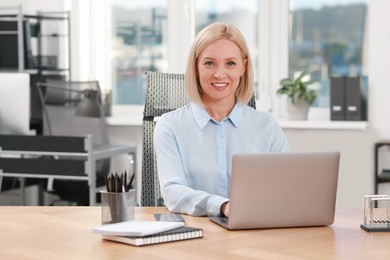 Photo of Portrait of smiling middle aged woman at table in office