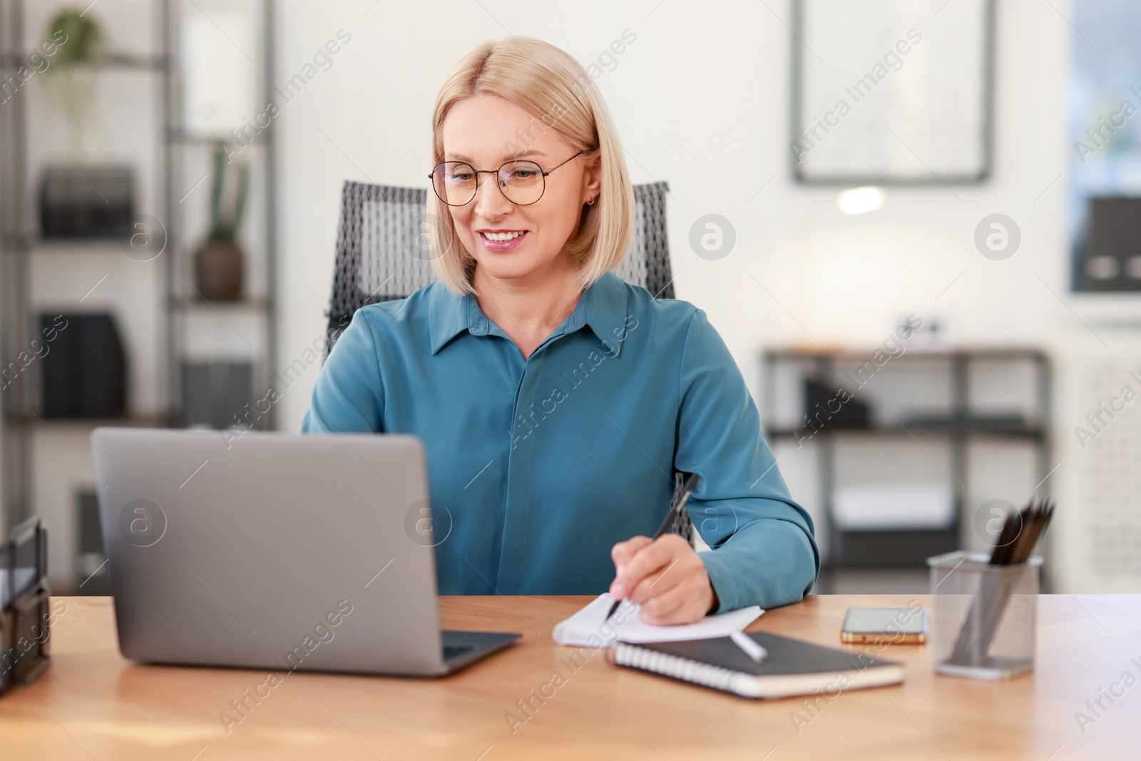 Photo of Smiling middle aged woman working with laptop at table in office