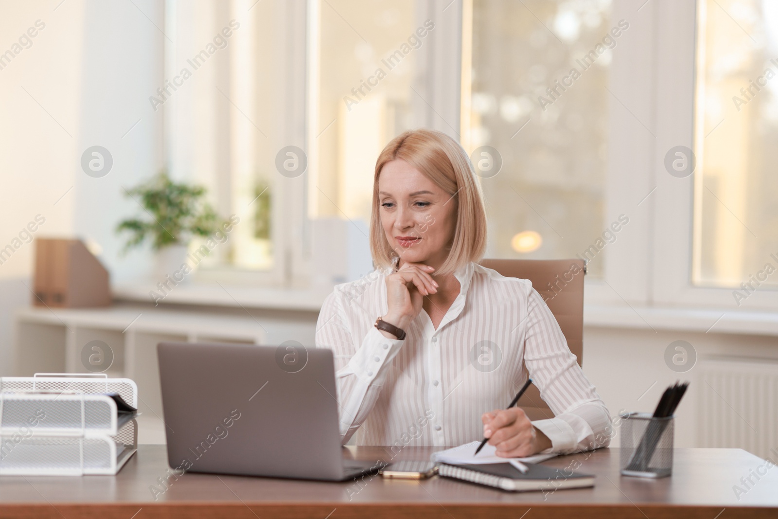 Photo of Middle aged woman working with laptop at table in office