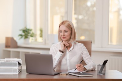 Middle aged woman working with laptop at table in office