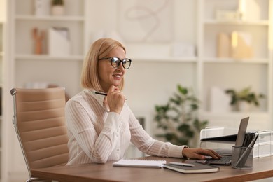 Photo of Smiling middle aged woman working with laptop at table in office