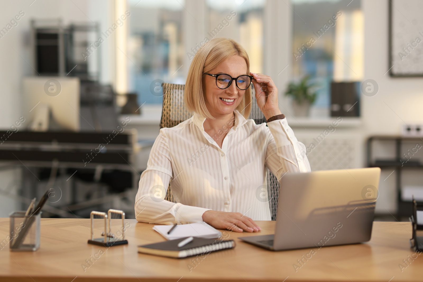 Photo of Smiling middle aged woman working with laptop at table in office