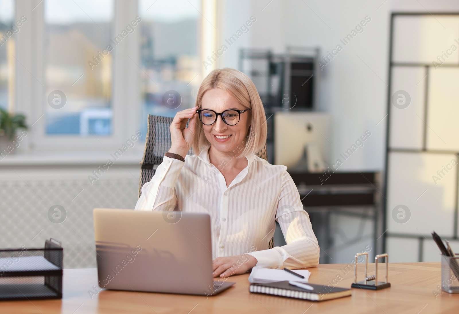 Photo of Smiling middle aged woman working with laptop at table in office