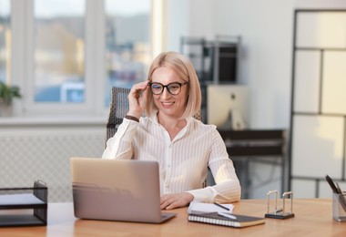 Photo of Smiling middle aged woman working with laptop at table in office