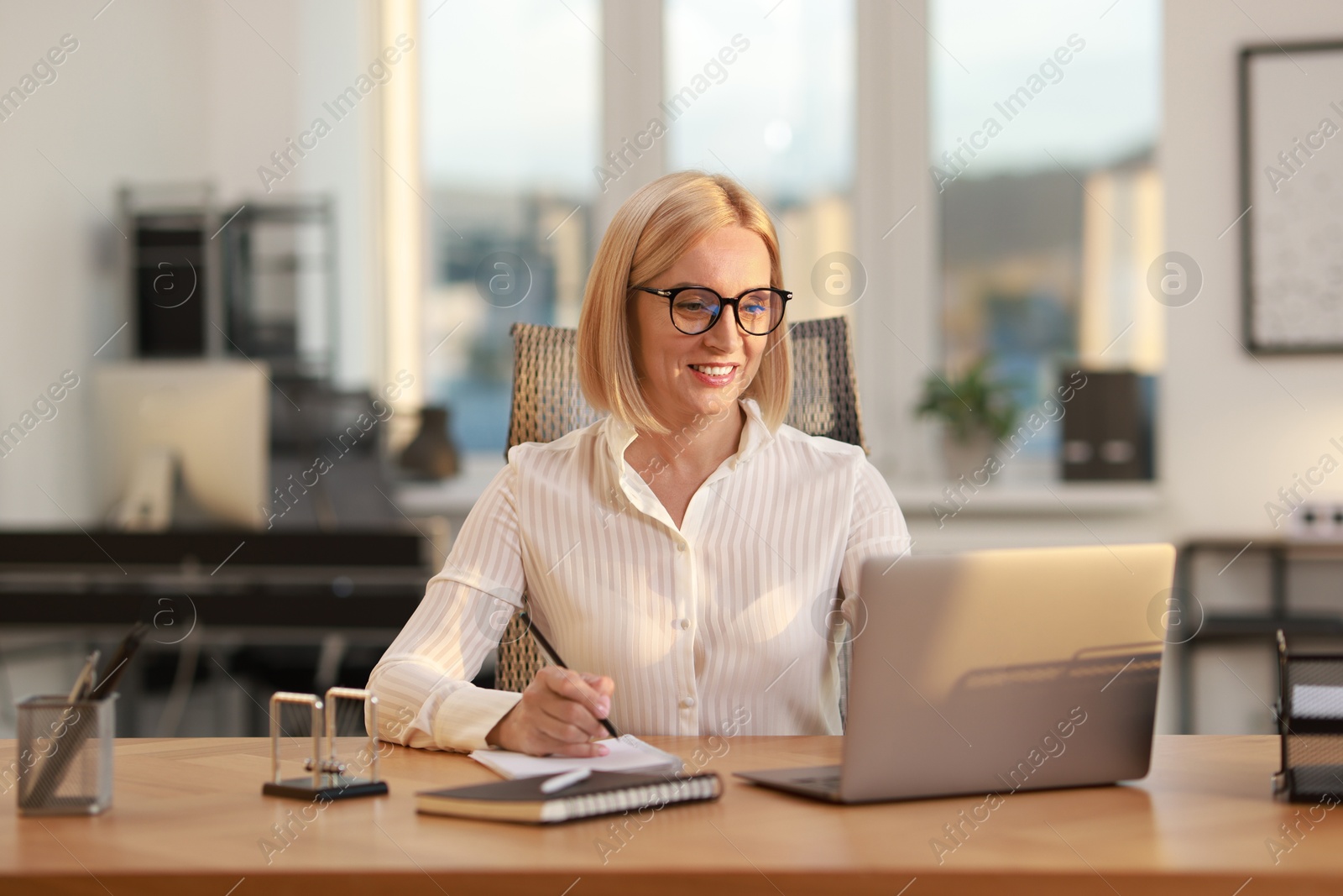 Photo of Smiling middle aged woman working with laptop at table in office