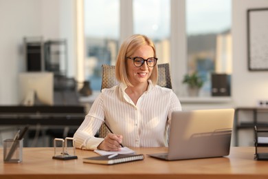 Photo of Smiling middle aged woman working with laptop at table in office