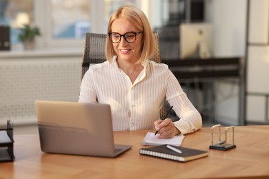 Photo of Smiling middle aged woman working with laptop at table in office