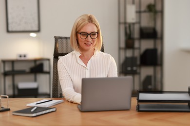 Photo of Smiling middle aged woman working with laptop at table in office