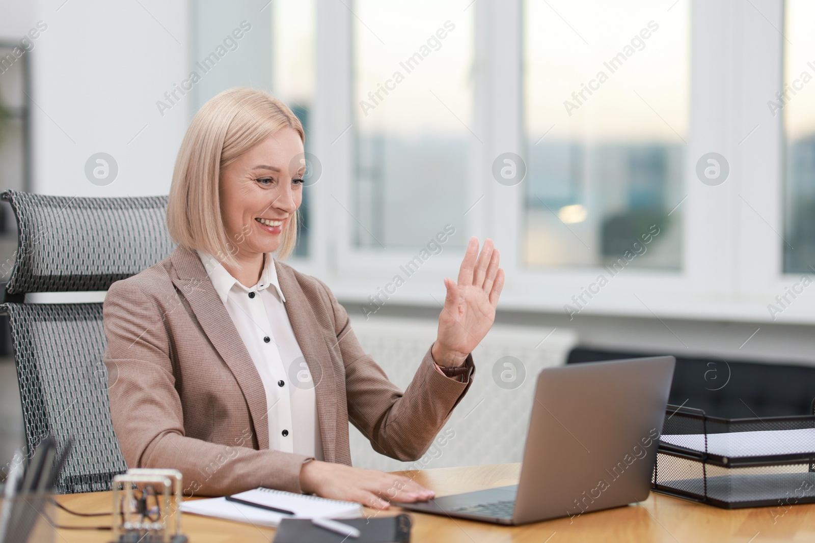 Photo of Smiling middle aged woman having videochat by laptop at table in office