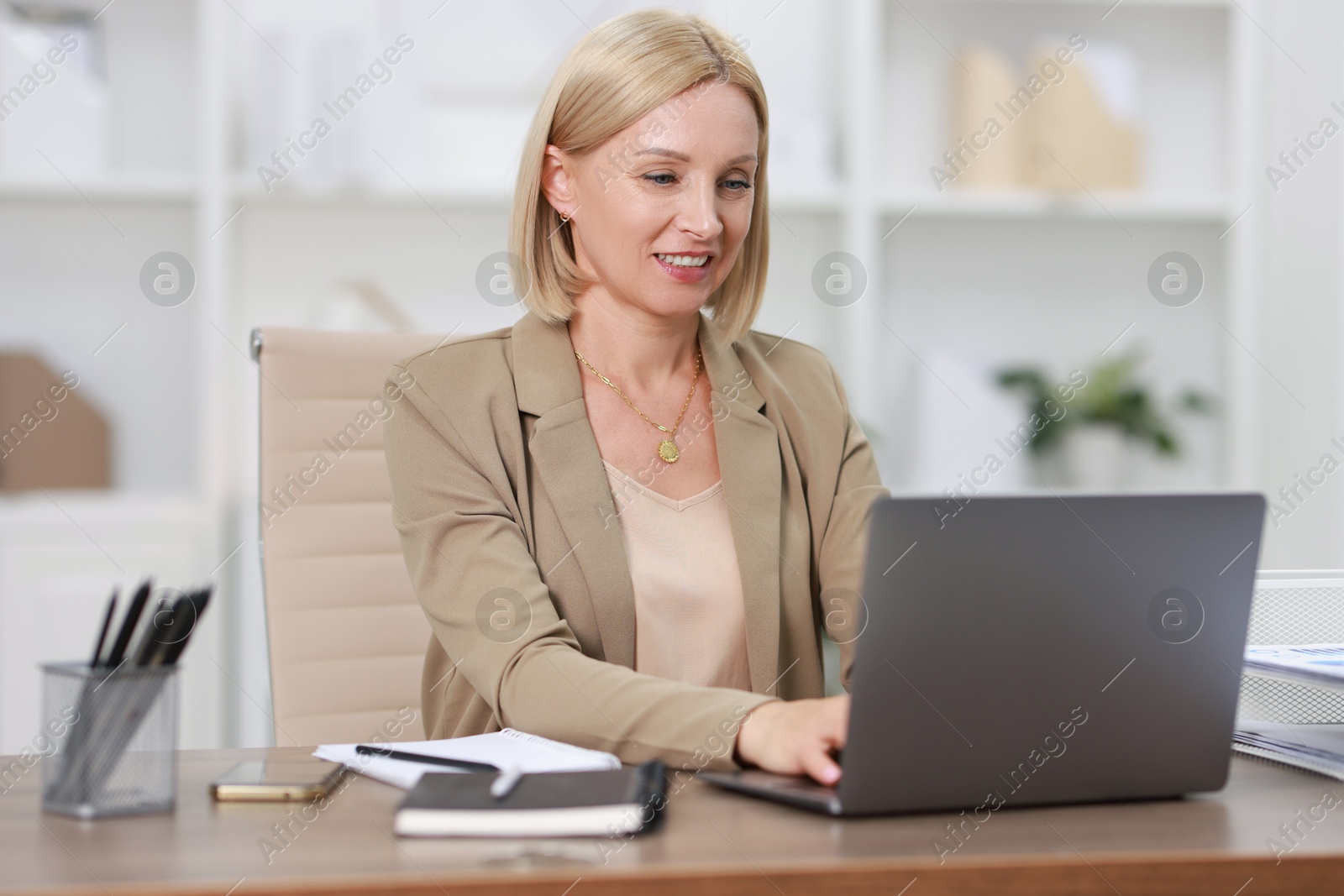 Photo of Smiling middle aged woman working with laptop at table in office