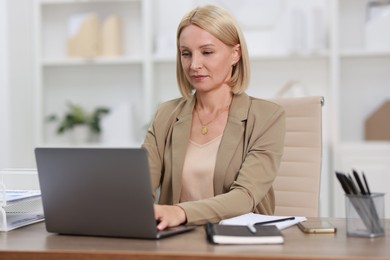 Photo of Middle aged woman working with laptop at table in office