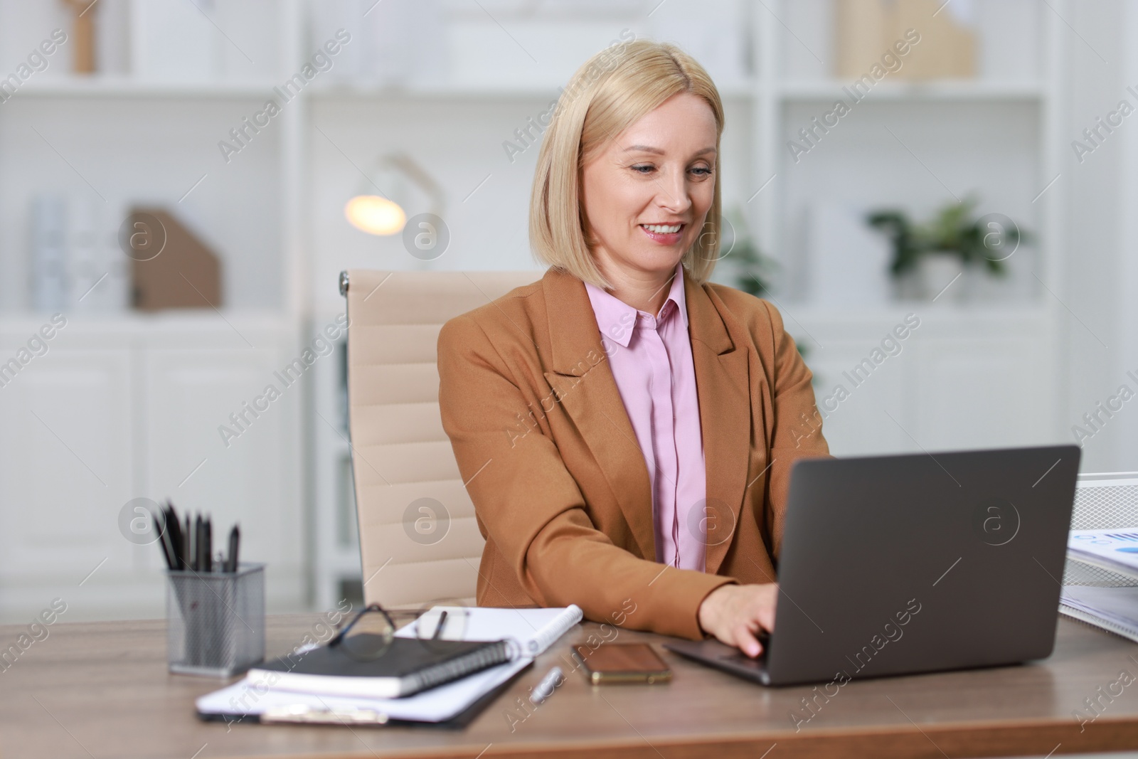 Photo of Smiling middle aged woman working with laptop at table in office