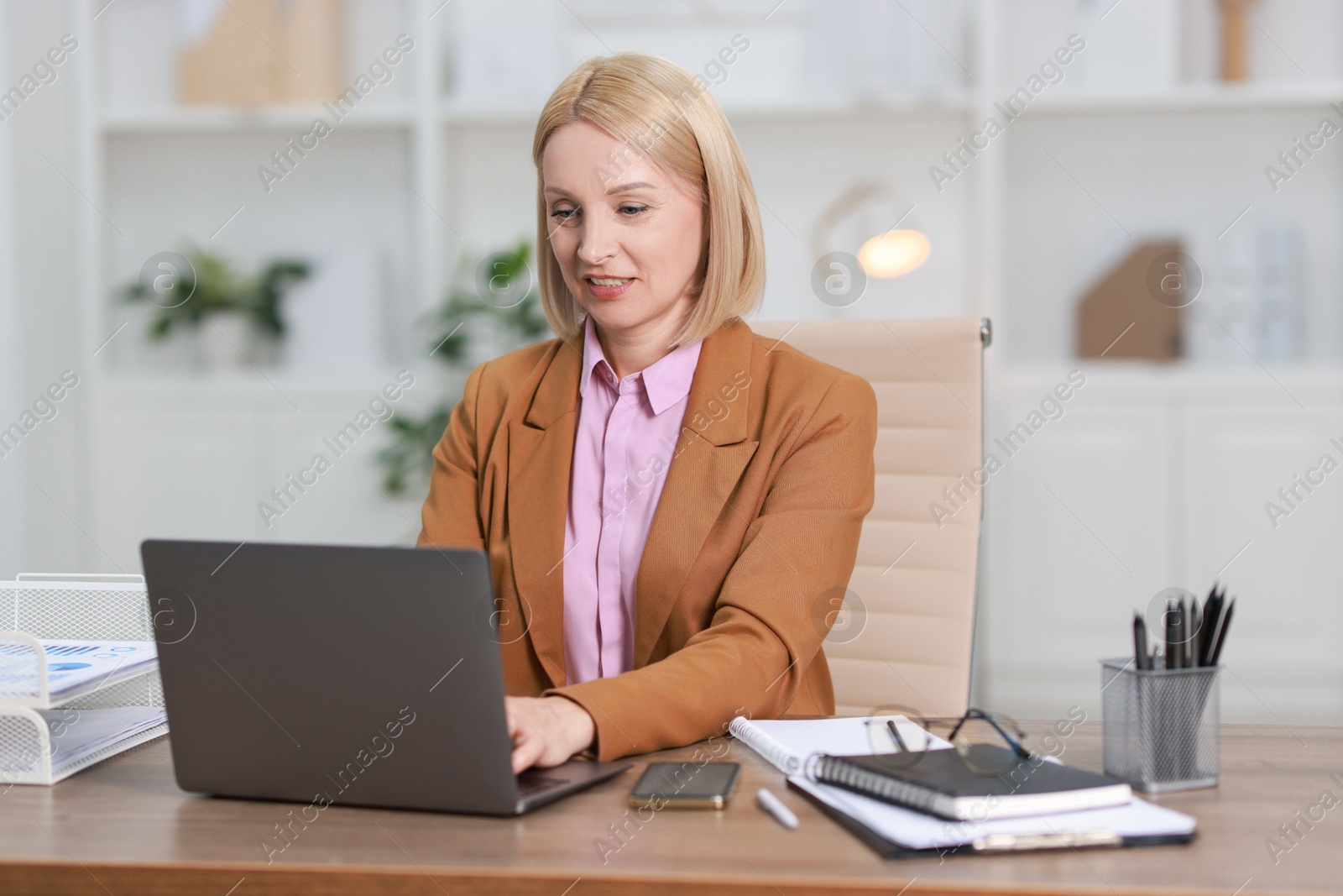 Photo of Middle aged woman working with laptop at table in office