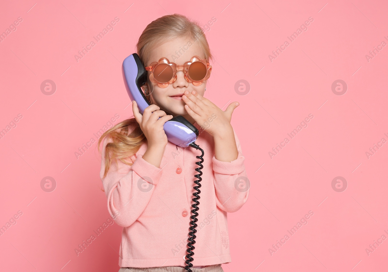 Photo of Cute little girl with handset of telephone on pink background