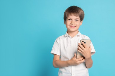 Cute little boy with smartphone on light blue background, space for text