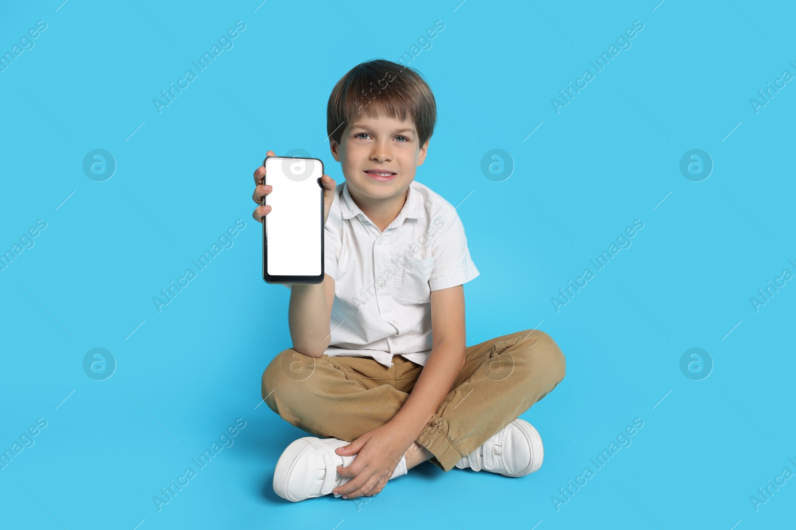 Photo of Cute little boy with smartphone on light blue background