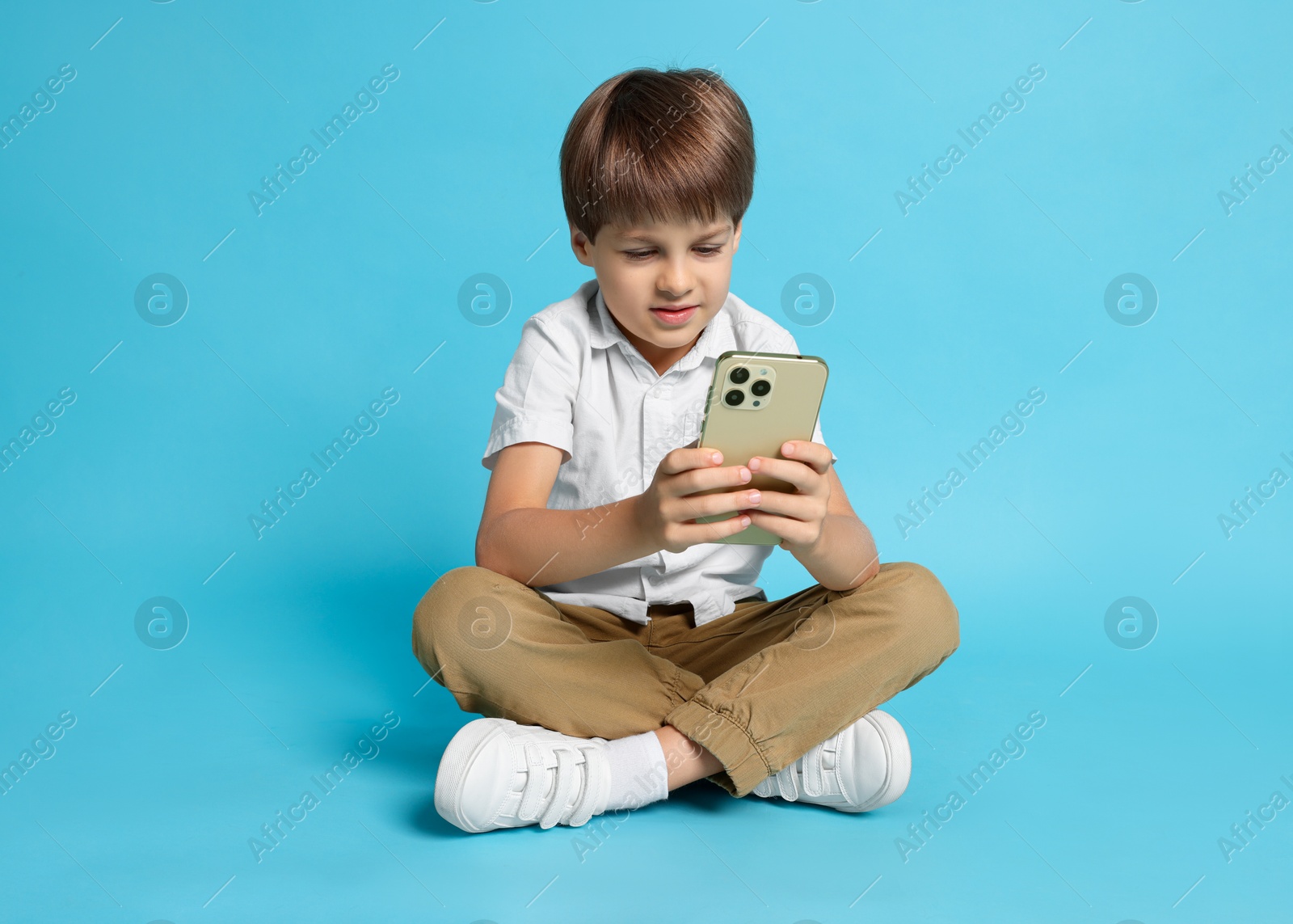 Photo of Cute little boy with smartphone on light blue background