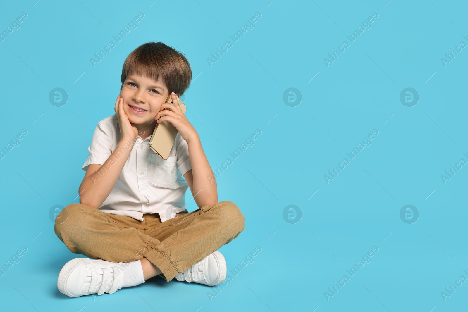 Photo of Cute little boy talking on smartphone against light blue background, space for text