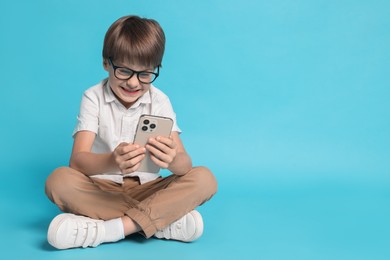 Photo of Cute little boy with smartphone on light blue background, space for text