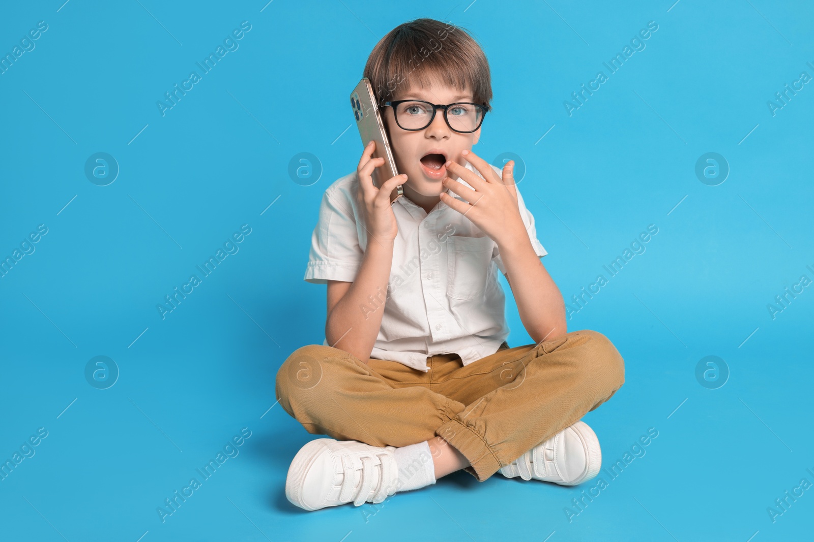 Photo of Cute little boy talking on smartphone against light blue background