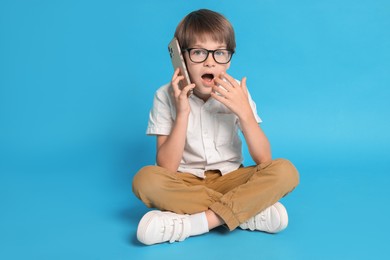 Photo of Cute little boy talking on smartphone against light blue background